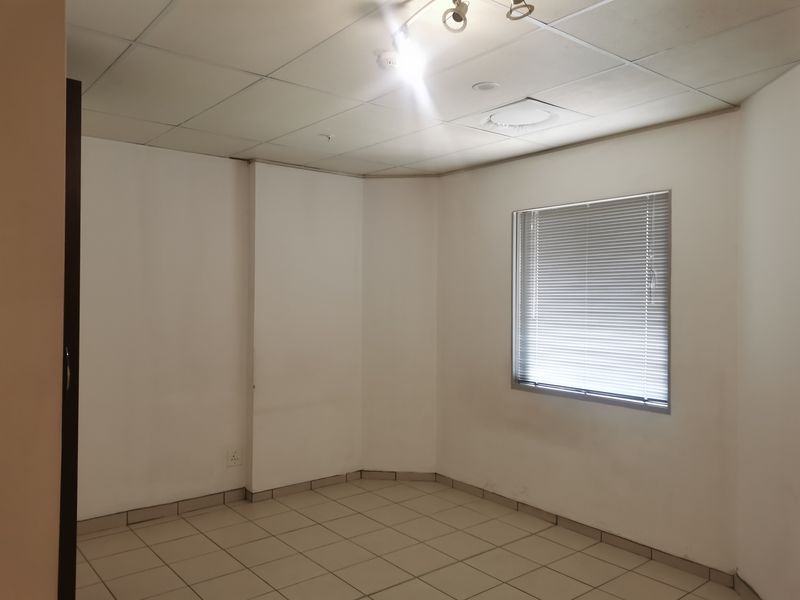 An empty bedroom featuring tiled flooring, a drop ceiling, and a window with fitted venetian blinds.