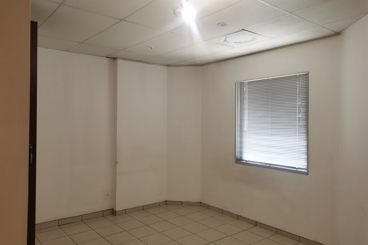 An empty bedroom featuring tiled flooring, a drop ceiling, and a window with fitted venetian blinds.