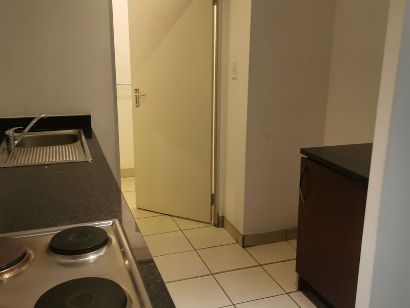 A functional kitchen area featuring dark granite countertops, a built-in electric hob, stainless steel sink, and tiled flooring with access to an adjacent room.