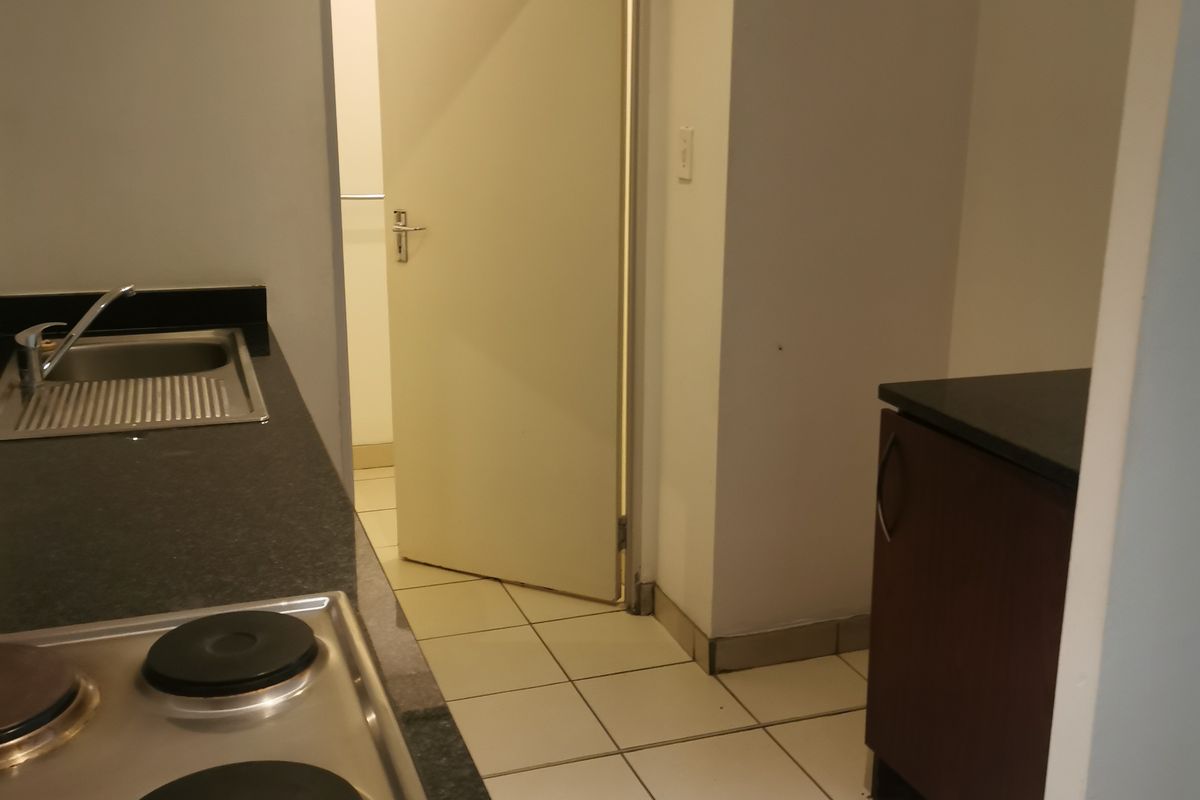 A functional kitchen area featuring dark granite countertops, a built-in electric hob, stainless steel sink, and tiled flooring with access to an adjacent room.
