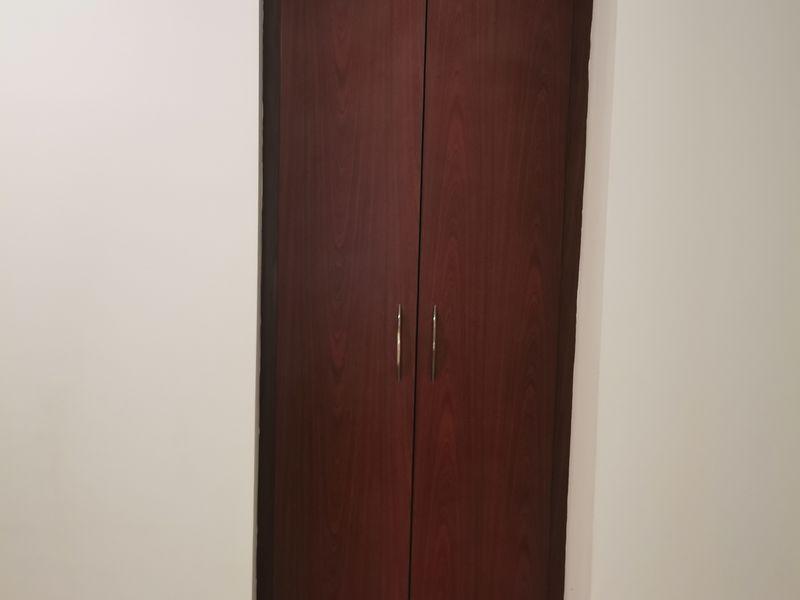 A simple bedroom interior featuring a dark wood built-in cupboard and neutral tiled flooring.