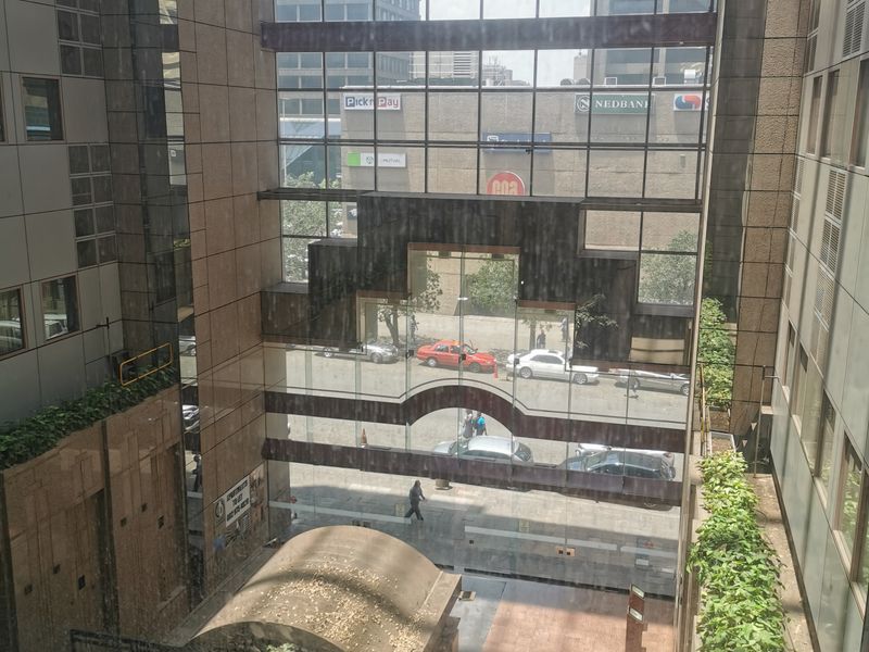A view looking out from an interior space through a large glass atrium facade towards the surrounding city street and buildings.