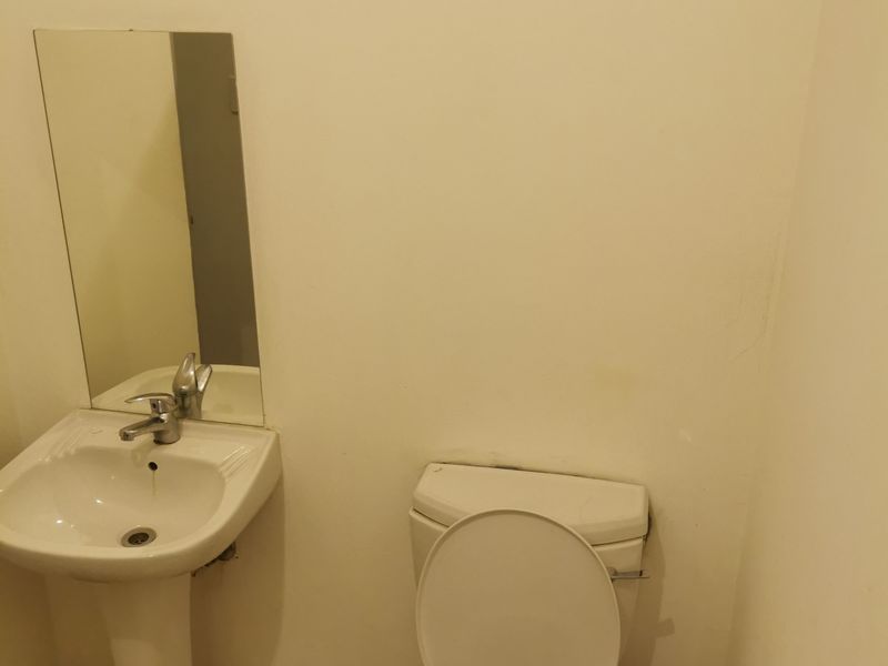 A compact bathroom featuring a pedestal basin, toilet, and wall-mounted mirror with tiled flooring.