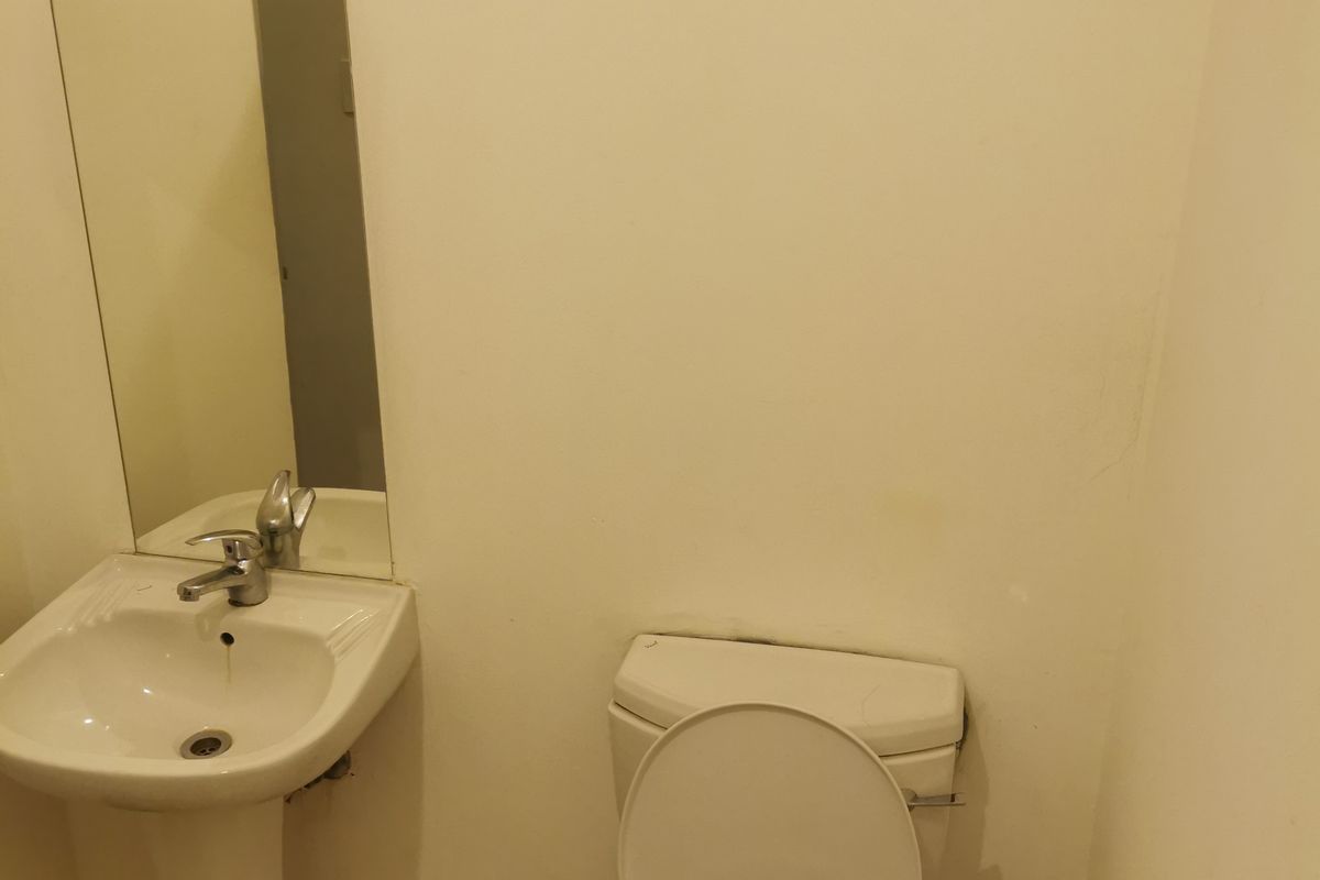A compact bathroom featuring a pedestal basin, toilet, and wall-mounted mirror with tiled flooring.