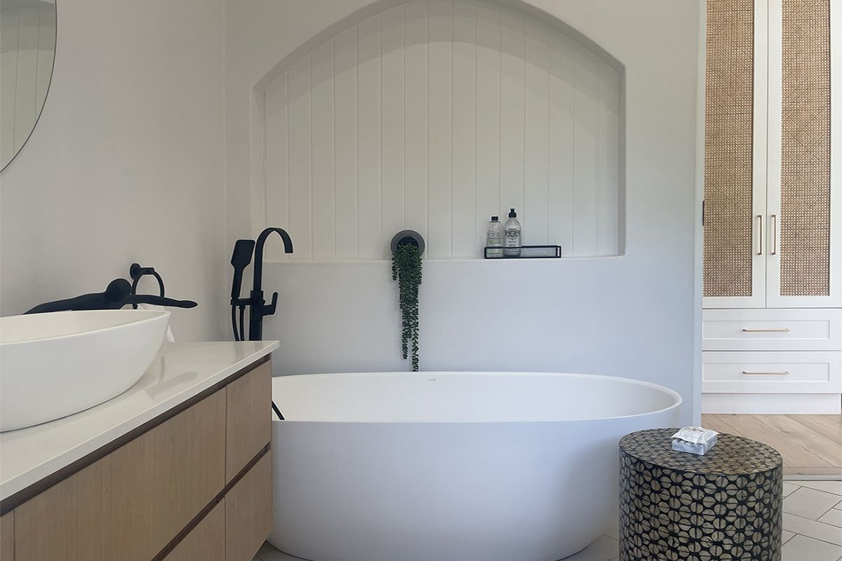 Modern bathroom featuring a freestanding bathtub, arched wall niche with paneling, matte black fixtures, and a floating timber vanity.
