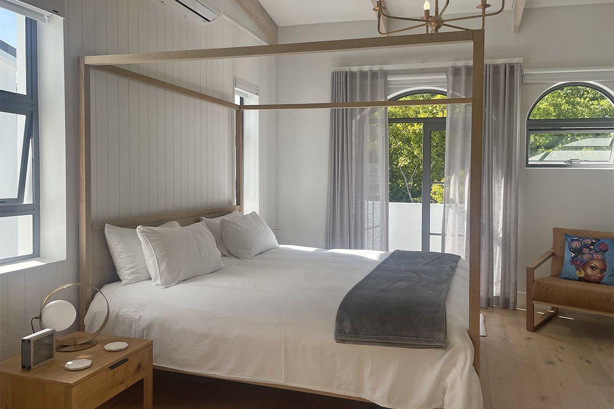 A bright and airy bedroom featuring timber flooring, vertical paneling, a split-system air conditioner, and arched windows with access to a balcony.