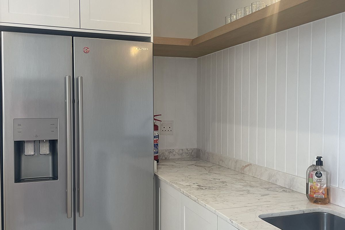 A modern kitchen area featuring white cabinetry, marble-look countertops, a double sink, and floating timber shelving with integrated lighting.