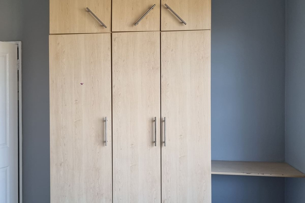 A bedroom featuring built-in light wood-finish cupboards with overhead storage and an integrated side shelf.