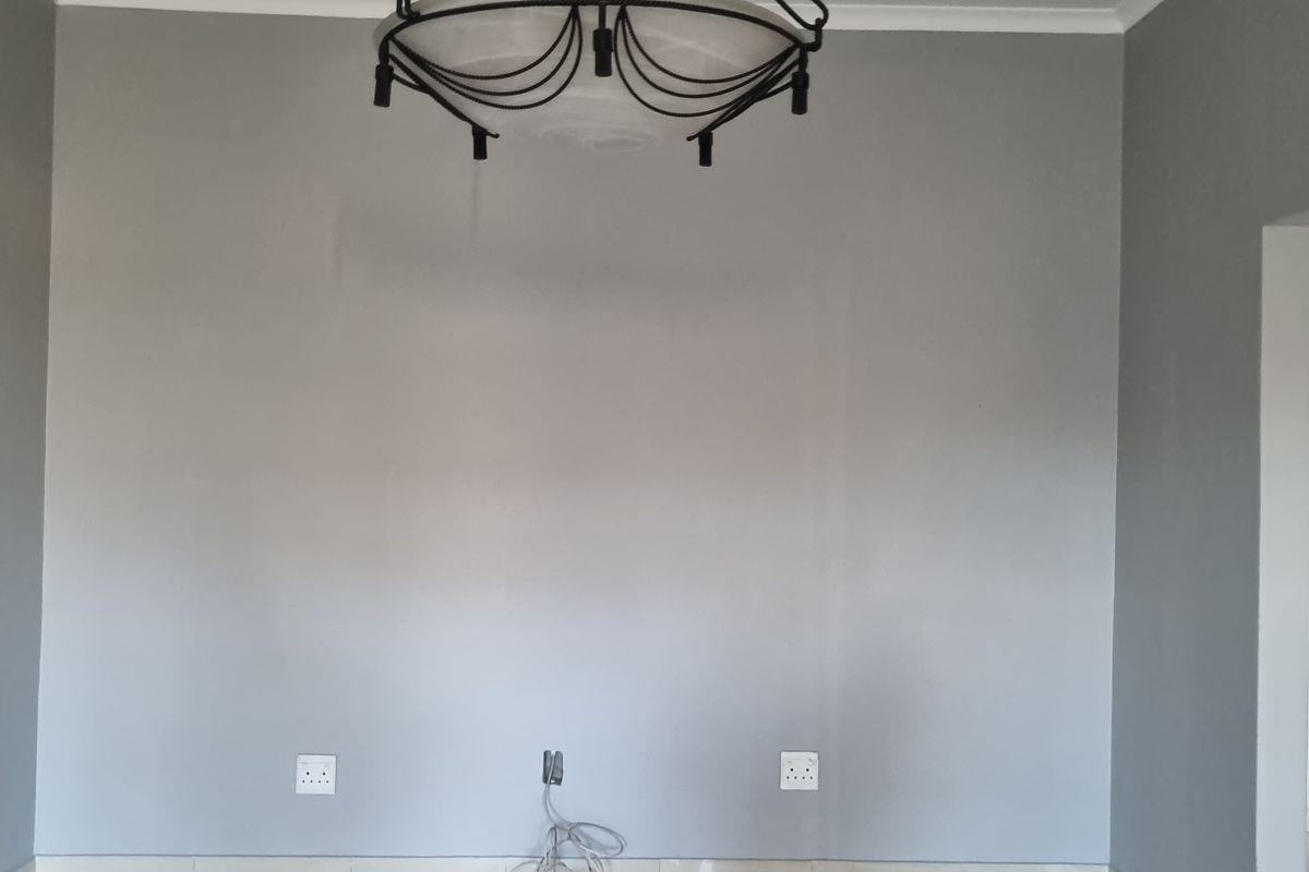 An empty living area featuring neutral grey walls, tiled flooring, and a decorative central pendant light fixture.