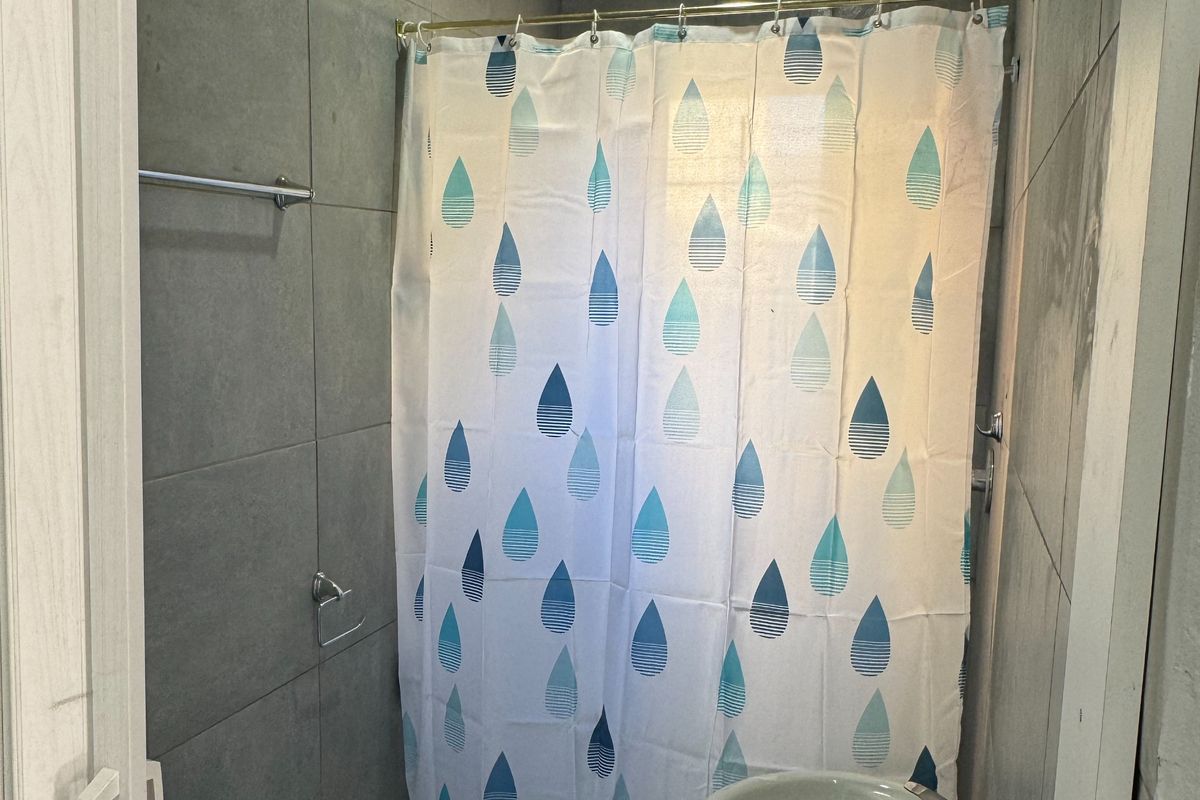 Compact bathroom featuring grey wall tiling, a pedestal basin, and a shower area with a curtain rail.