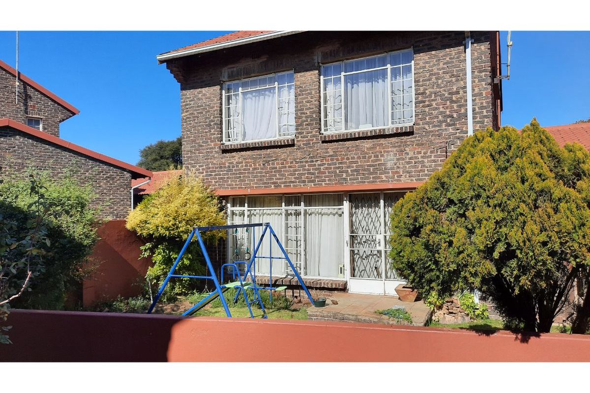 Rear view of a double-story brick townhouse featuring a small garden, paved patio area, and secure access points.