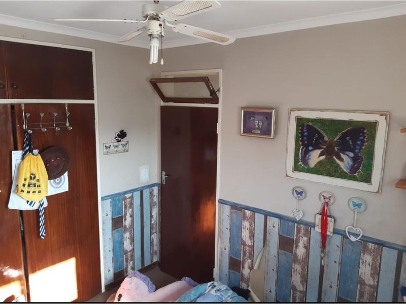 Bedroom featuring built-in wardrobe storage, a ceiling fan, and decorative wall paneling with a traditional timber door and transom window.