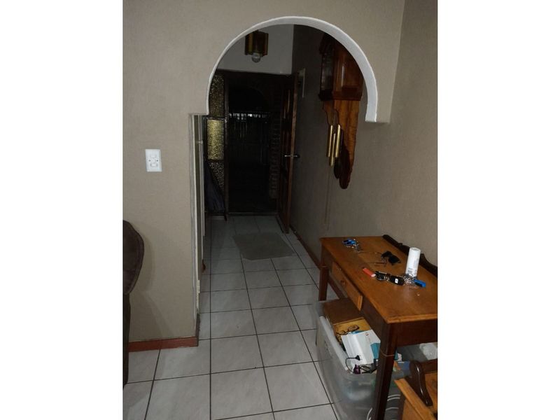 A tiled hallway featuring an arched architectural doorway leading to an adjacent room, with neutral wall finishes.