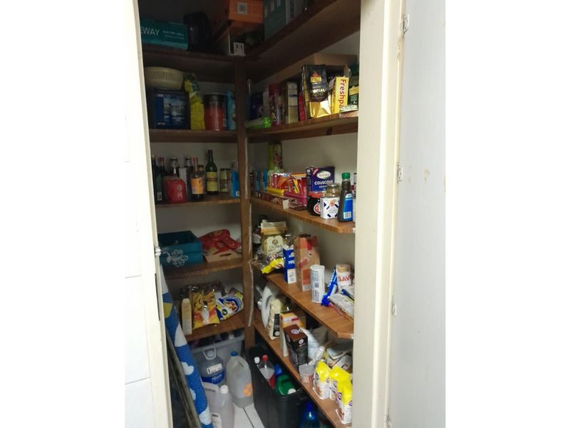 A functional walk-in pantry or scullery storage area featuring multiple built-in wooden shelves for organized storage.