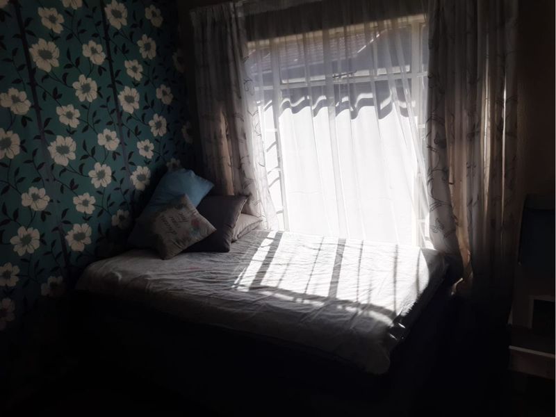 A bedroom featuring a window with curtain tracks and patterned wallpaper, receiving natural light.