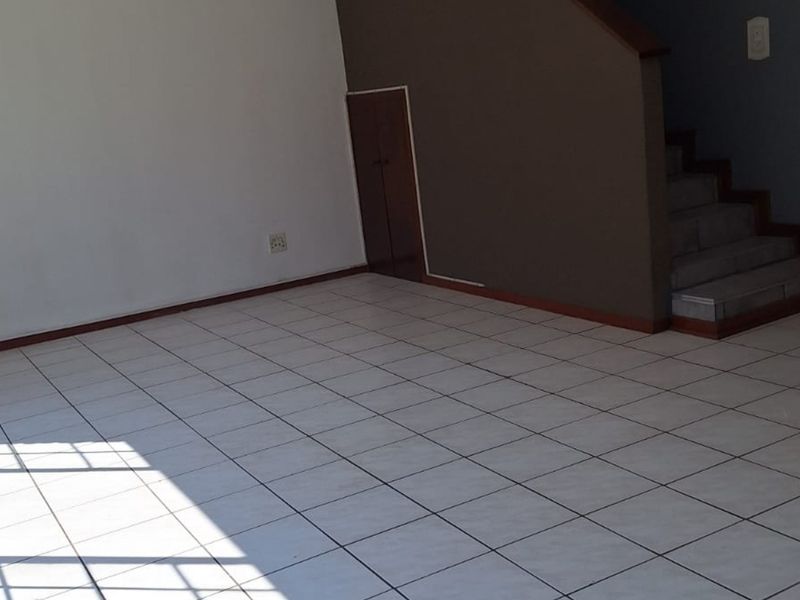 An empty living area featuring tiled flooring, a staircase with under-stair storage, and neutral wall finishes.