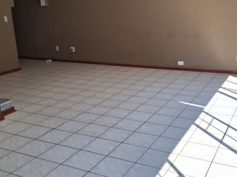 An empty, open-plan living area featuring neutral-toned walls and light-colored ceramic floor tiles with natural light streaming in.