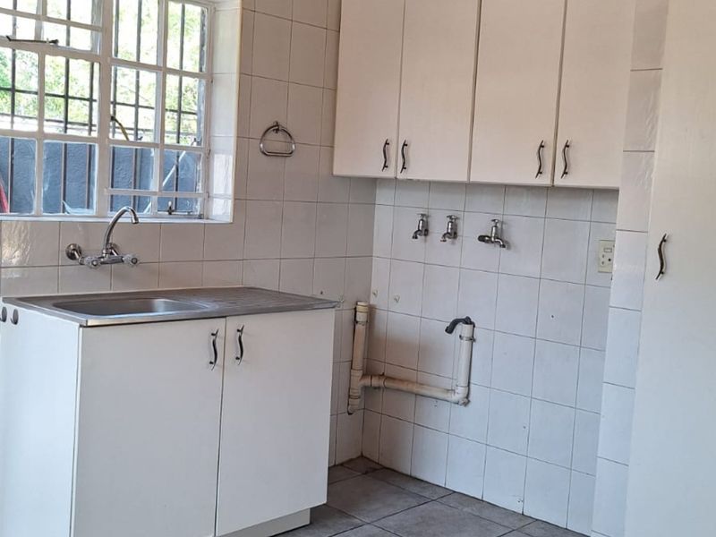 A functional laundry area featuring built-in cabinetry, a stainless steel sink, and tiled splashbacks with dedicated plumbing connections for appliances.