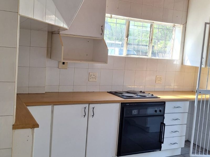 A functional kitchen featuring white cabinetry, a laminate countertop, built-in oven and hob, and tiled backsplash, ready for a modern update.