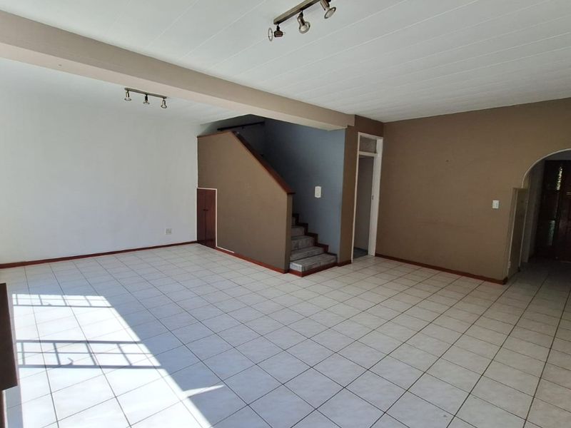 Spacious, empty living area featuring tiled flooring, a central staircase with under-stair storage, and an arched entryway leading to the front door.