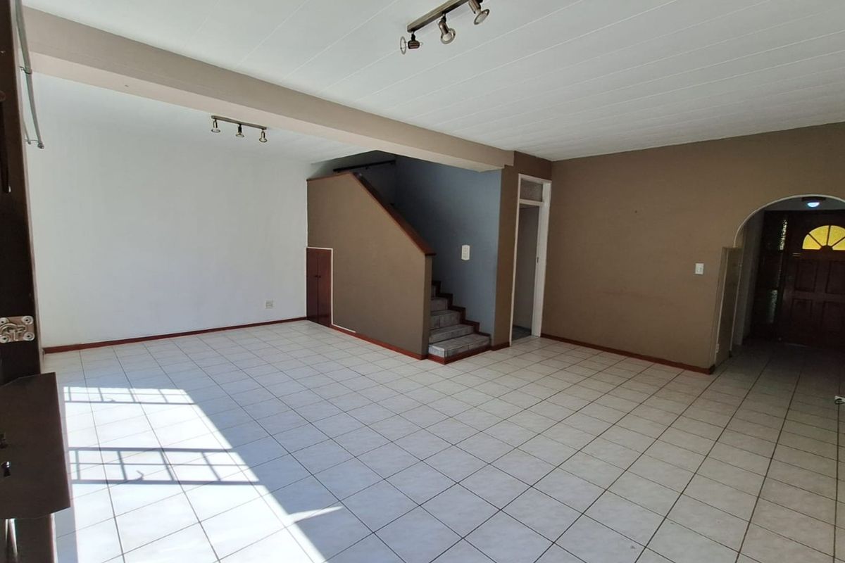 Spacious, empty living area featuring tiled flooring, a central staircase with under-stair storage, and an arched entryway leading to the front door.