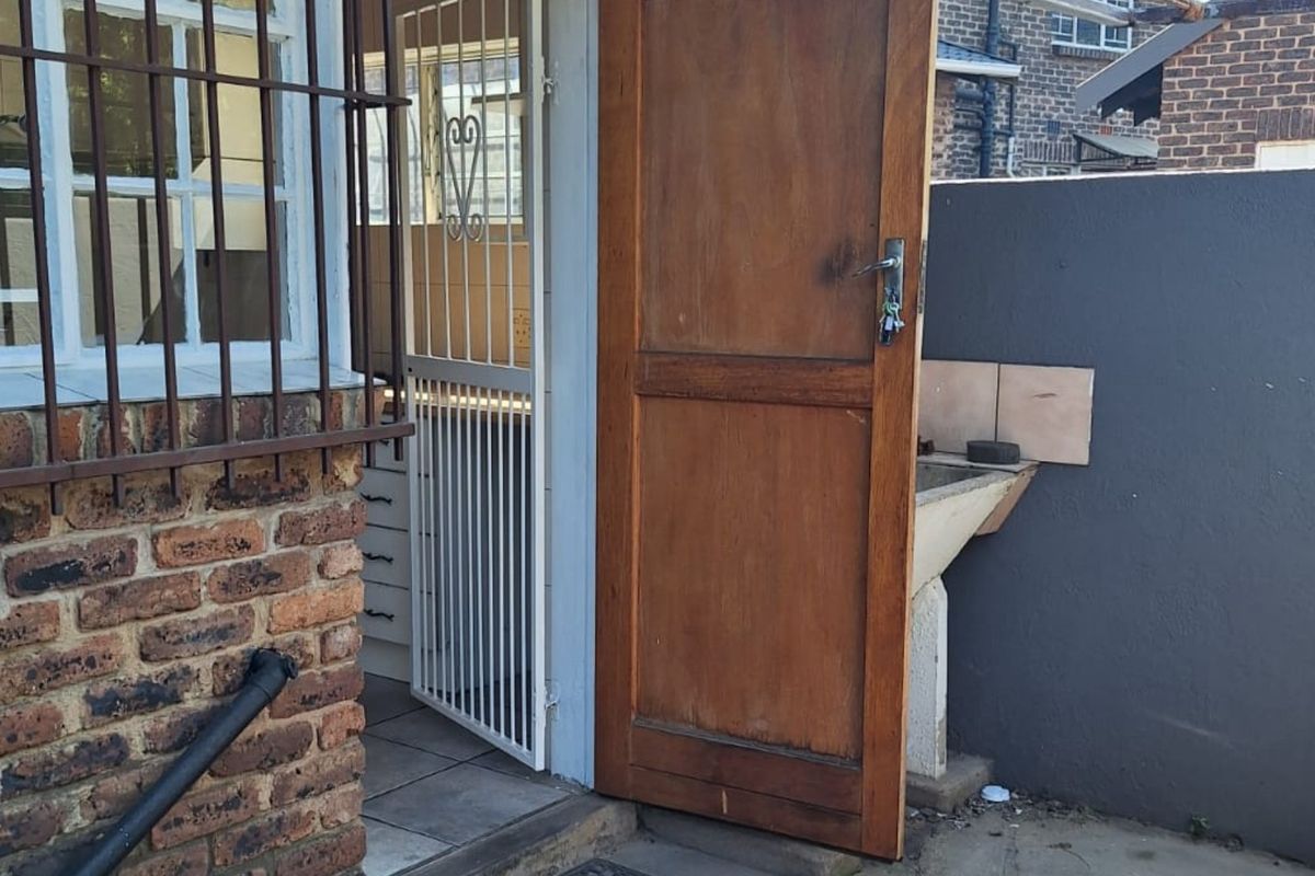 Rear exterior area featuring a brick facade, security gate, timber door, and a fixed concrete utility sink.