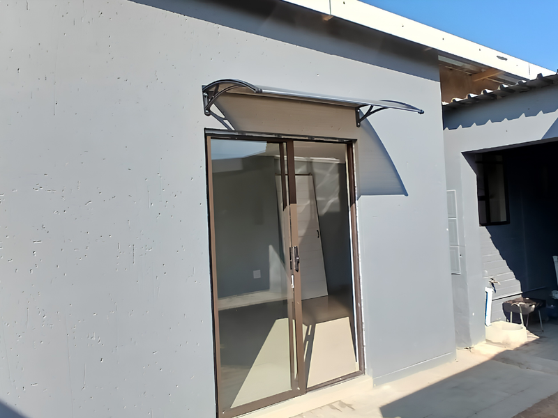 Rear exterior view of the cottage featuring a sliding glass door with a protective awning and an adjacent covered patio area.