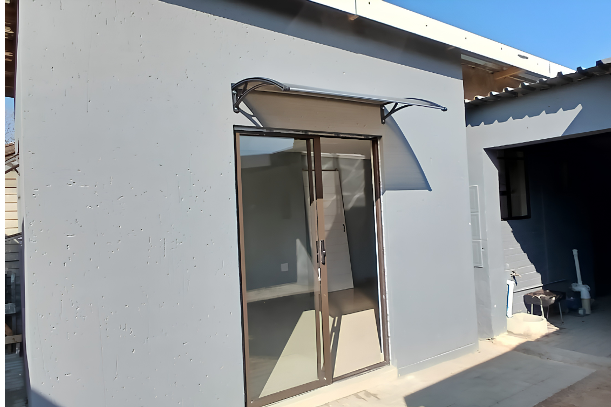 Rear exterior view of the cottage featuring a sliding glass door with a protective awning and an adjacent covered patio area.
