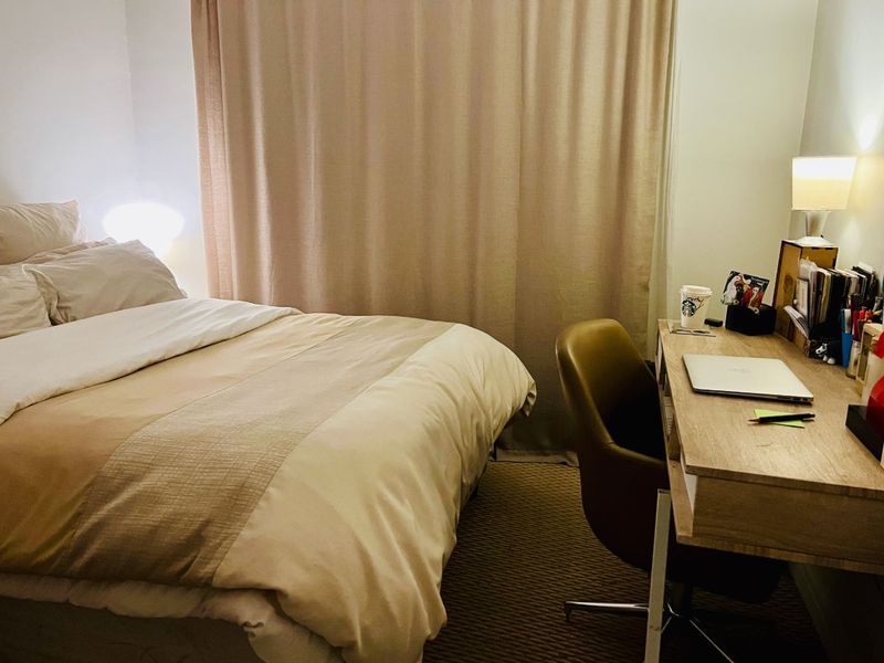 A functional bedroom featuring neutral tones, carpeted flooring, and floor-to-ceiling curtains, providing a comfortable and private sleeping space.