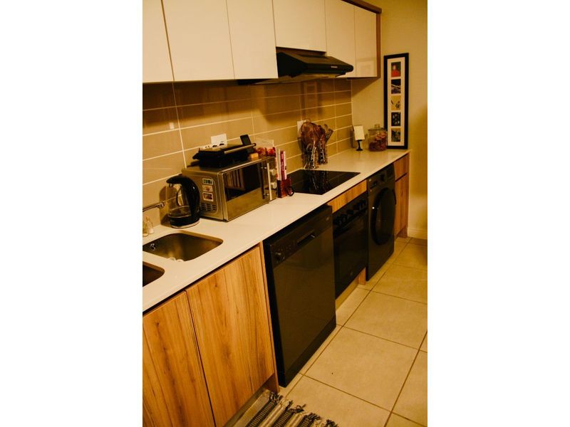A compact kitchen featuring modern wood-finish cabinetry, white countertops, a tiled backsplash, and integrated appliances including a hob, oven, and dishwasher.
