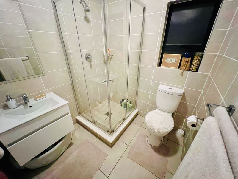A compact, modern bathroom featuring a glass shower enclosure, wall-mounted vanity with basin, and a standard toilet with neutral wall and floor tiling.