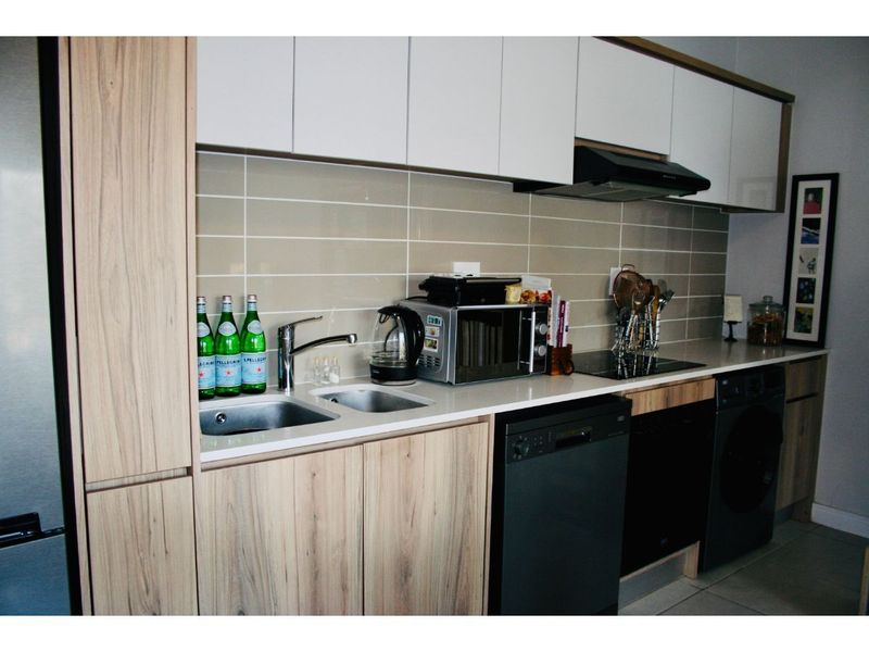 Modern kitchen featuring light wood-grain cabinetry, white stone countertops, a tiled backsplash, and integrated appliances including a dishwasher and hob.