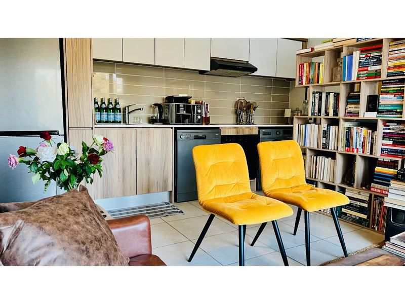 A modern open-plan kitchen area featuring wood-grain cabinetry, integrated appliances, tiled backsplash, and extensive built-in shelving, seamlessly connected to the living space.