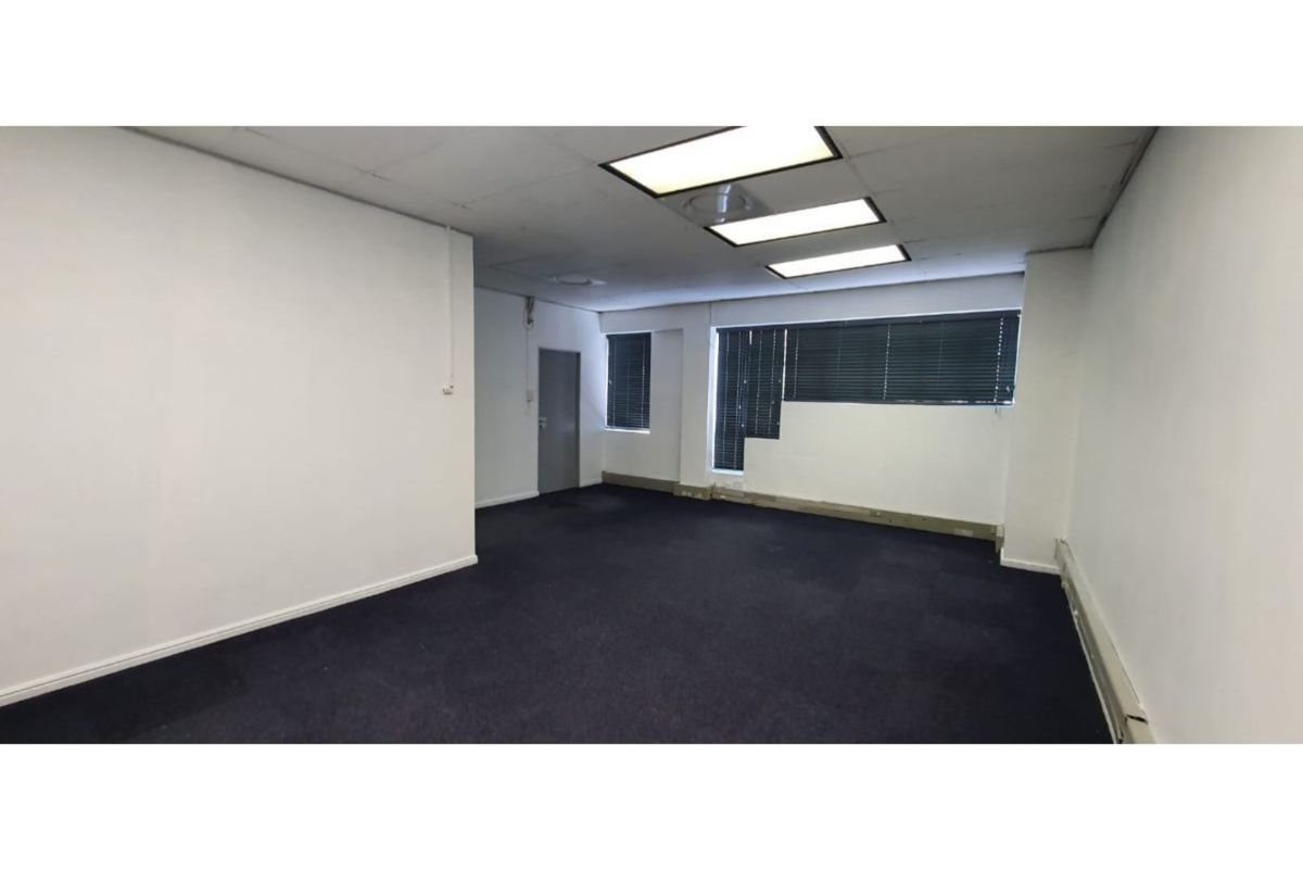 An empty office space featuring dark carpeting, recessed ceiling lighting, and venetian blinds, providing a blank canvas for professional workspace customization.