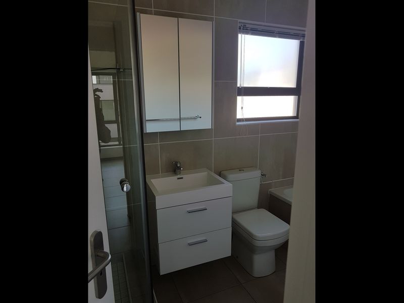 Modern bathroom featuring a wall-mounted vanity, mirrored medicine cabinet, glass shower enclosure, and neutral floor-to-ceiling tiling.