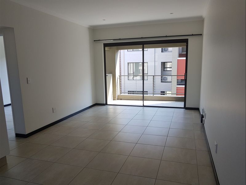A bright, empty living room featuring neutral tiled flooring and a large sliding glass door that opens onto a private balcony.