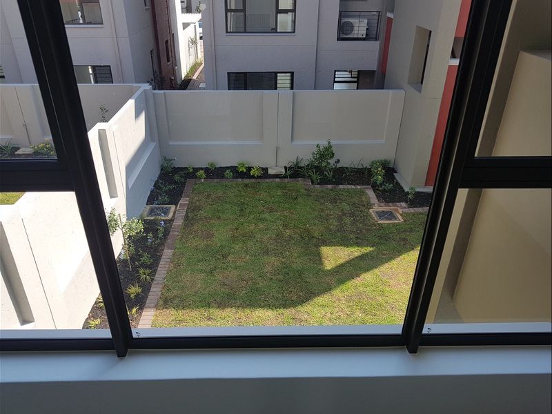 A view from an elevated position overlooking a private rear garden with a lawn, brick edging, and perimeter boundary walls.