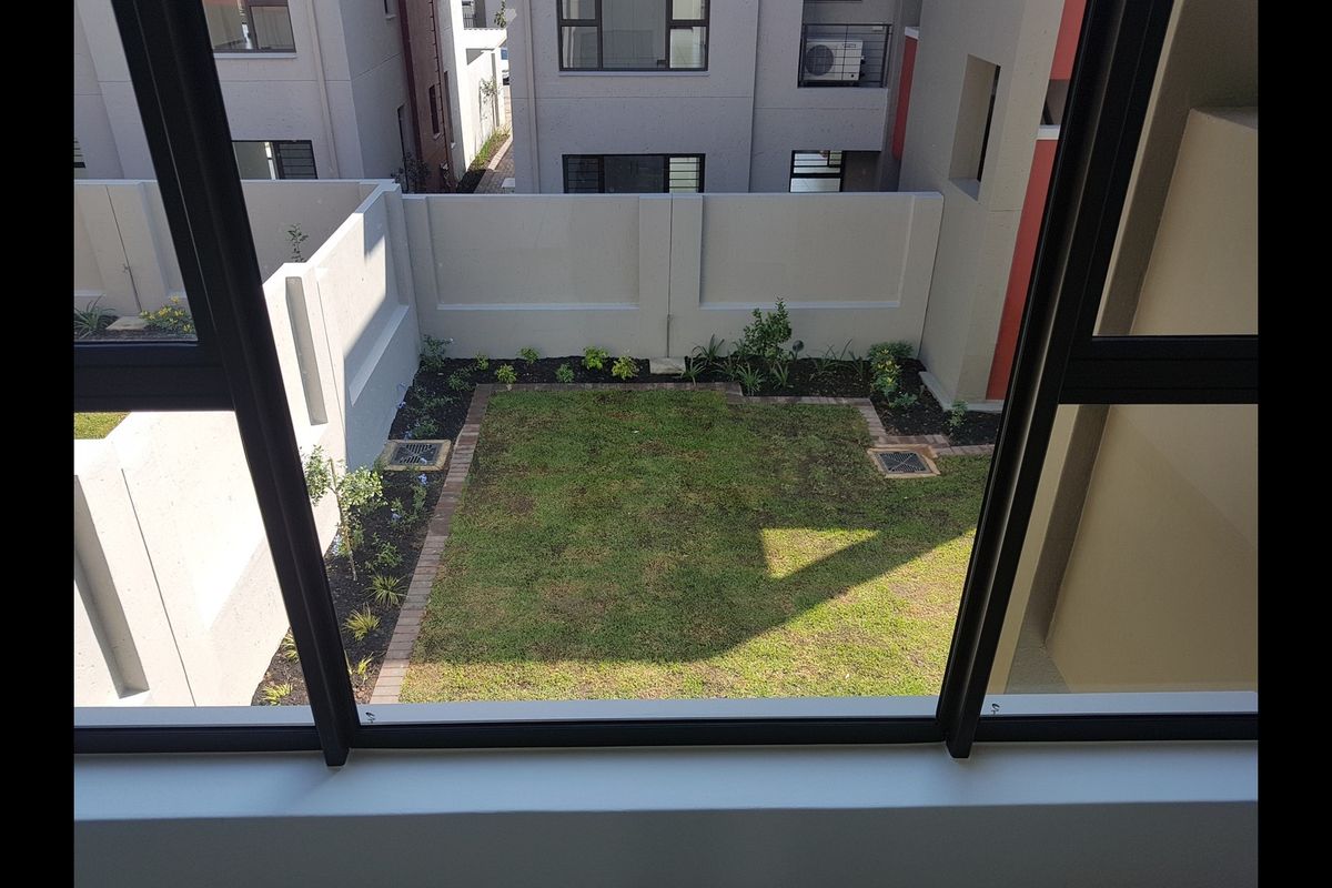 A view from an elevated position overlooking a private rear garden with a lawn, brick edging, and perimeter boundary walls.