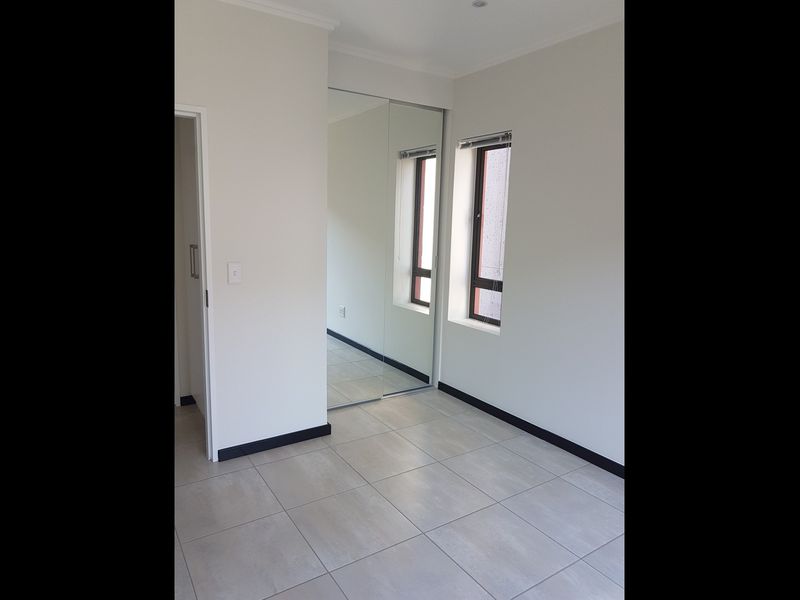 A clean, empty bedroom featuring neutral tiled flooring, built-in mirrored wardrobes, and modern aluminium-framed windows.