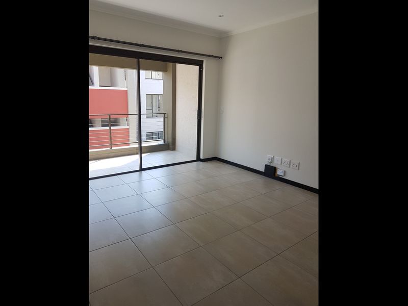 An empty, well-maintained living area featuring neutral tiled flooring and a large sliding glass door providing access to an outdoor balcony.