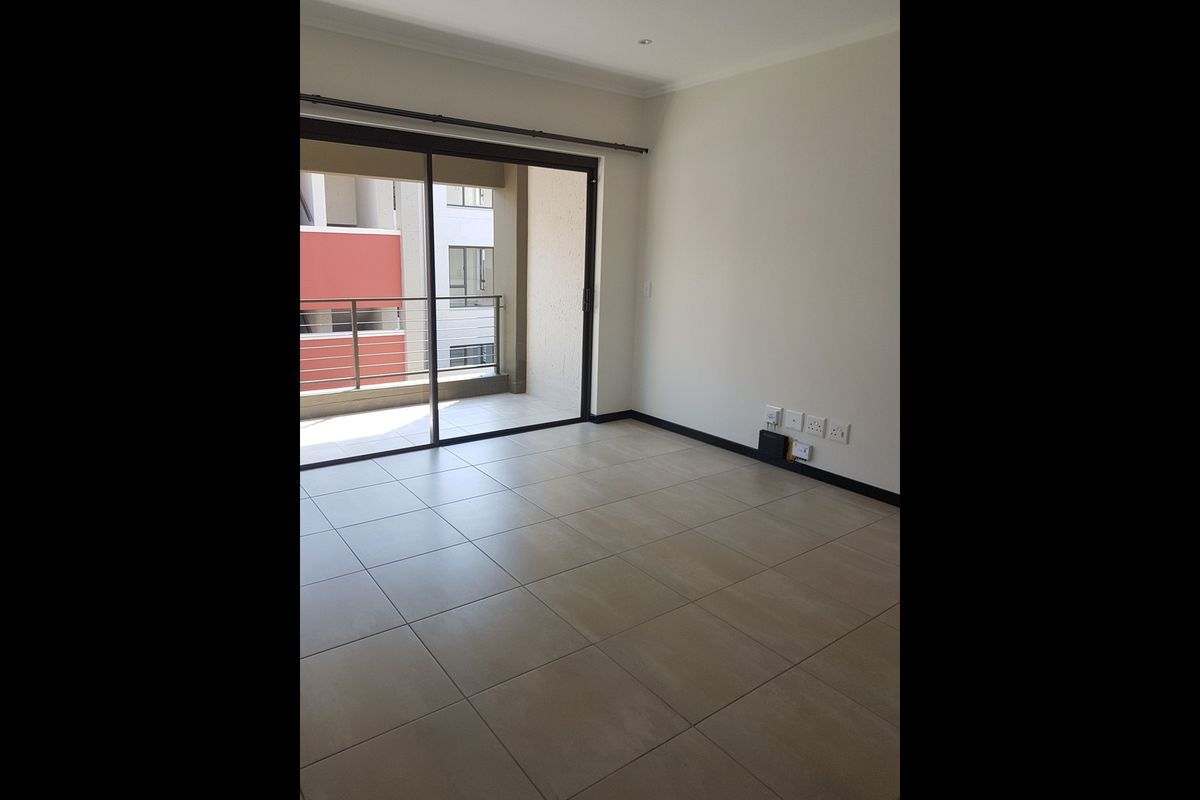 An empty, well-maintained living area featuring neutral tiled flooring and a large sliding glass door providing access to an outdoor balcony.