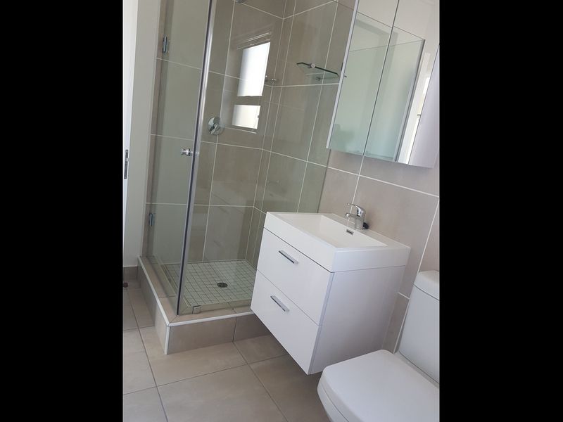 Modern bathroom featuring a glass shower enclosure, wall-mounted vanity with basin, and neutral tiled finishes throughout.
