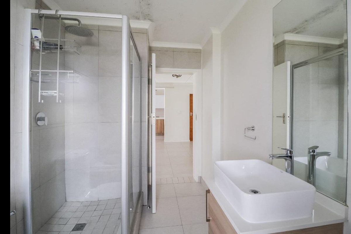 Bathroom featuring a glass shower enclosure, modern vanity basin with cabinet, and wall mirror. Note visible ceiling water staining requiring attention.