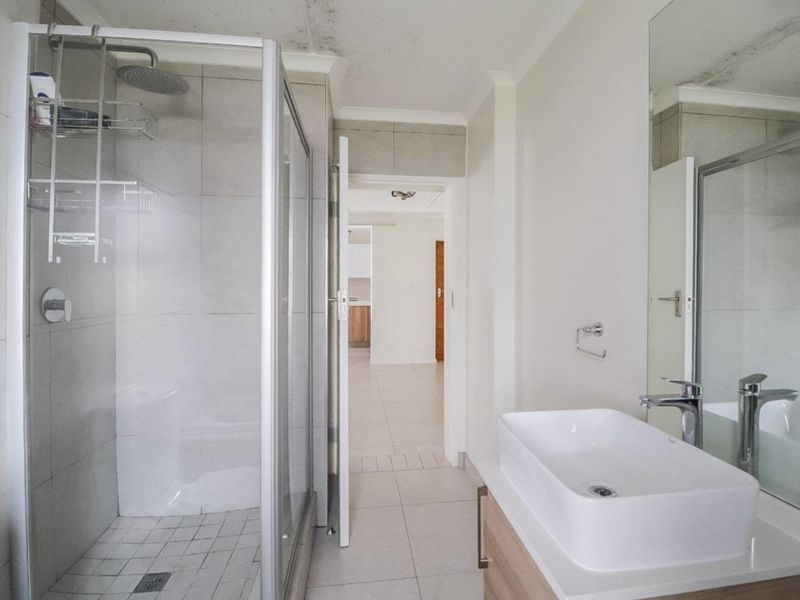 Bathroom featuring a glass shower enclosure, modern vanity basin with cabinet, and wall mirror. Note visible ceiling water staining requiring attention.
