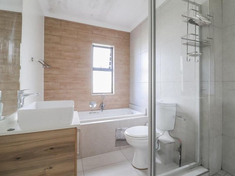 Modern bathroom featuring a built-in vanity with vessel sink, separate bathtub, and glass-enclosed shower with neutral tile finishes.