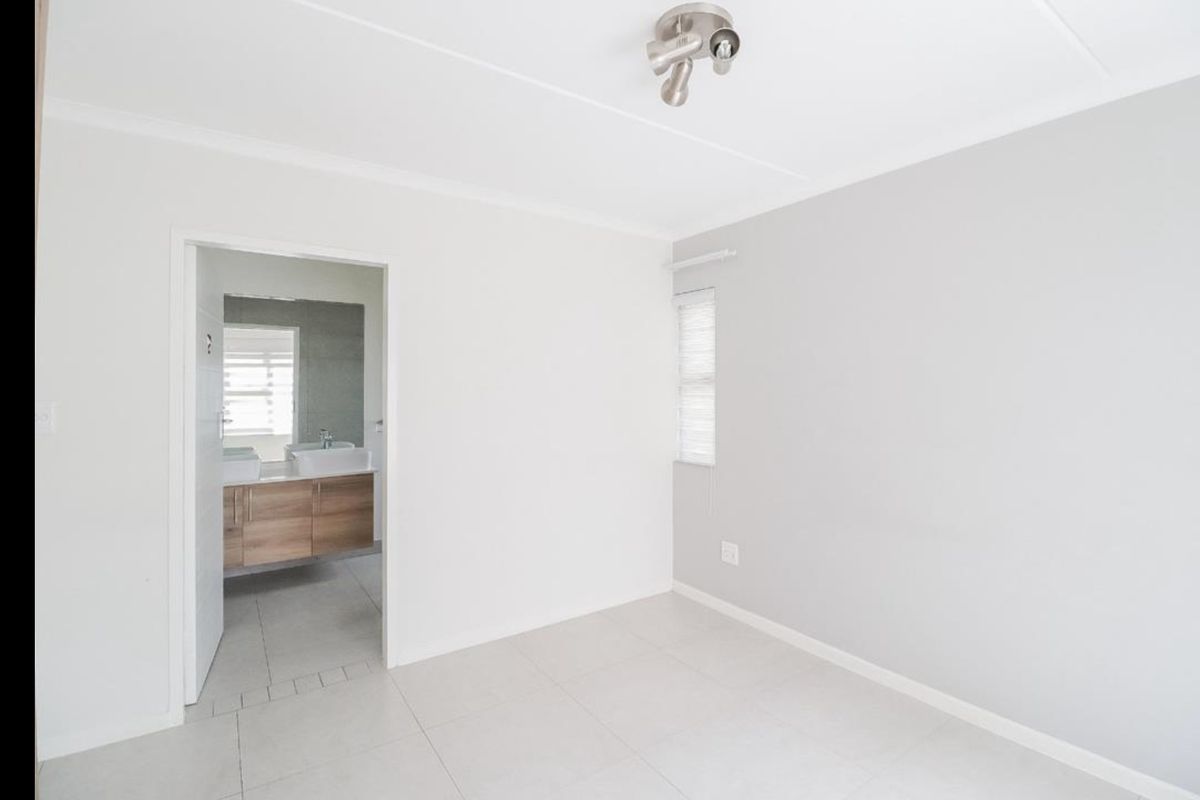 A bright, empty bedroom featuring neutral tiled flooring, clean white walls, and direct access to an en-suite bathroom.