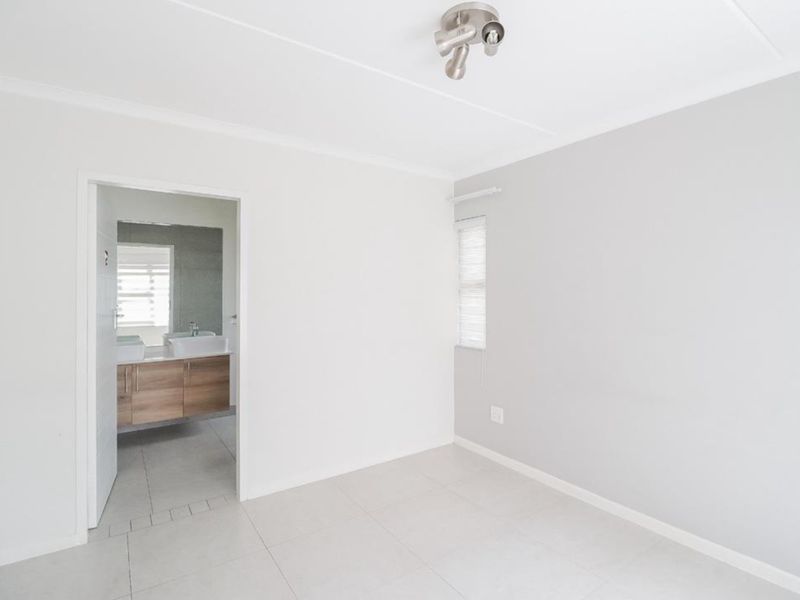 A bright, empty bedroom featuring neutral tiled flooring, clean white walls, and direct access to an en-suite bathroom.