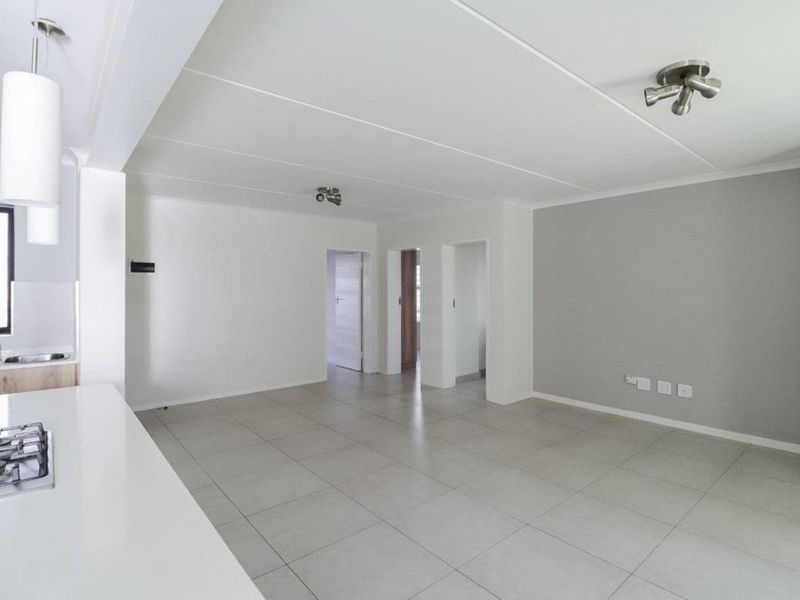 Spacious open-plan living area featuring neutral tiled flooring, modern recessed lighting, and a functional kitchen space with a built-in gas hob.