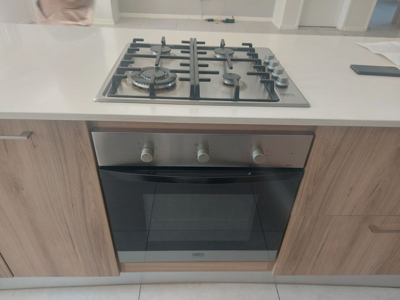 Modern kitchen island featuring a stainless steel gas cooktop and built-in oven with light wood-grain cabinetry and stone countertops.