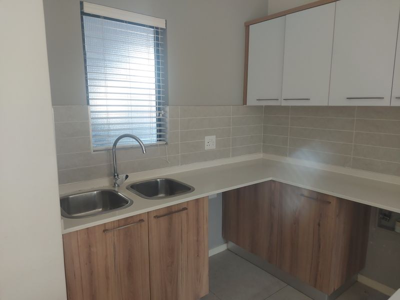 A clean, modern kitchen featuring double stainless steel sinks, wood-finish cabinetry, and neutral tiled splashbacks, offering a functional and well-maintained workspace.